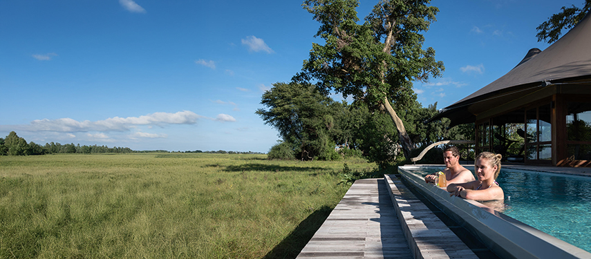 Two guests look out over the grassy plains of the Okavango Delta from an infinity pool at a luxury safaro camp in Botswana