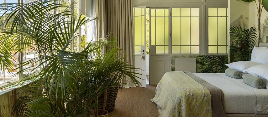 Botanical-themed bedroom at Dorp Hotel filled with greenery and sunlight streaming through French doors.