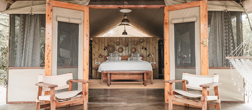 View into a tented suite with wooden doors open to reveal a king-sized bed and armchairs.