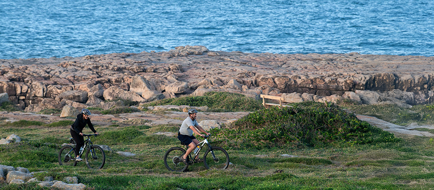 Guests cycling along the rocky coastline with the ocean in the background.