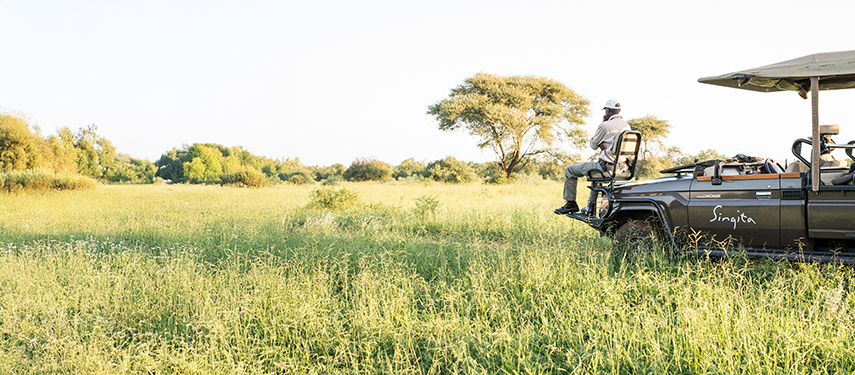 Game drive vehicle in lush grassy plains with a spotter seated on the front