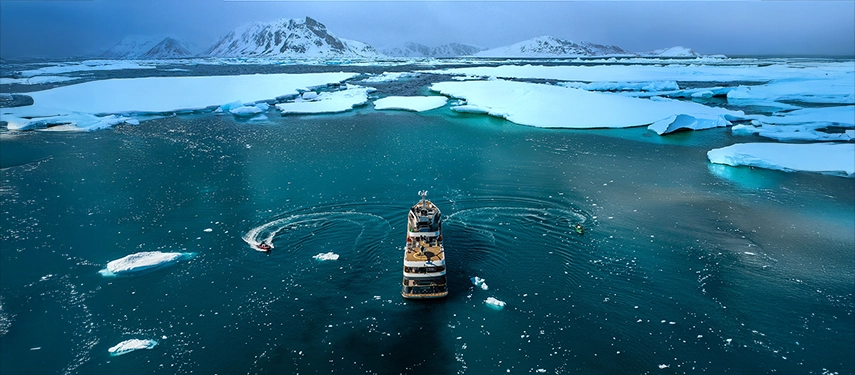 Aqua Lares navigating through icy Arctic waters surrounded by snow-covered mountains.
