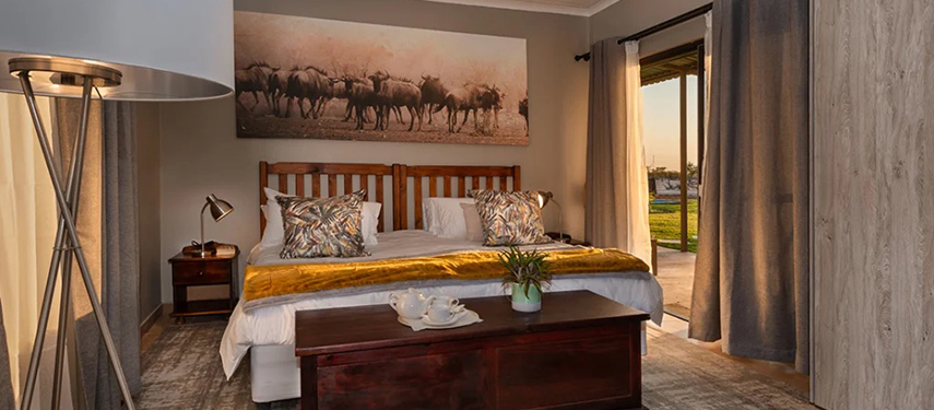 A Safari House bedroom featuring a king-size bed, earthy tones, and doors opening onto a lawn.