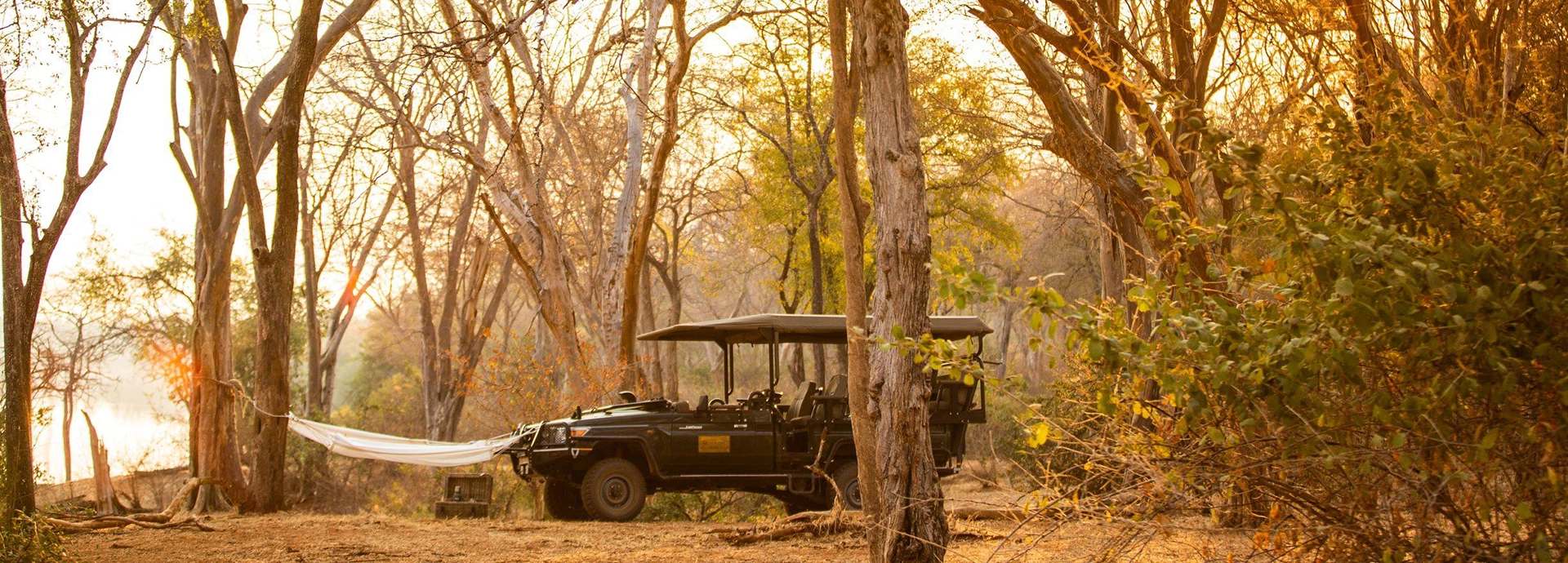 A game vehicle rests amongst winterthorn trees with a hammock and bush lunch nearby.