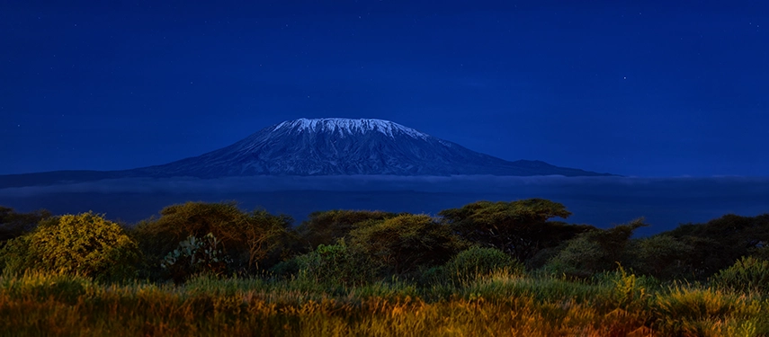Distant view of Mount Kilimanjaro rising above a band of low-lying clouds under a twilight sky.