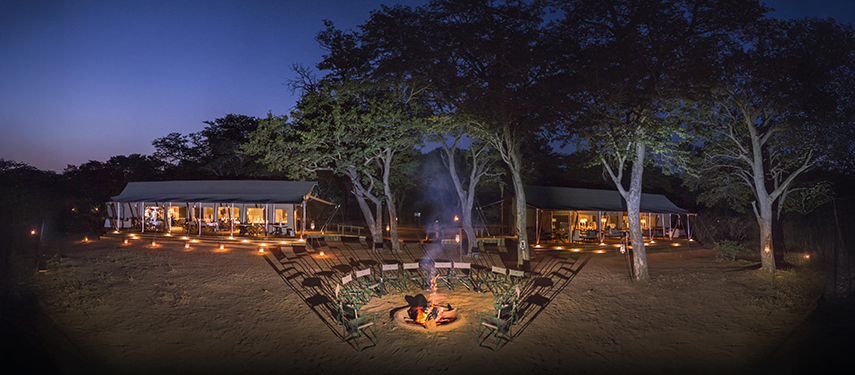 Twilight aerial perspective of Verney’s Camp featuring campfire seating and tented pavilions among the trees.
