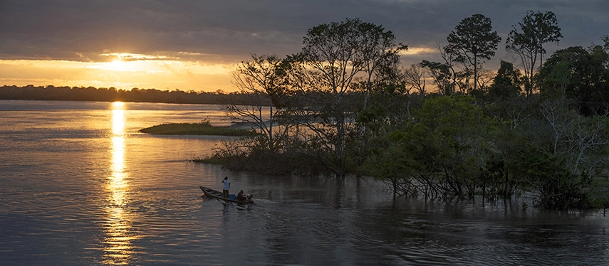 Golden sunset over the Peruvian Amazon, with a lone fisherman paddling across still reflective waters.