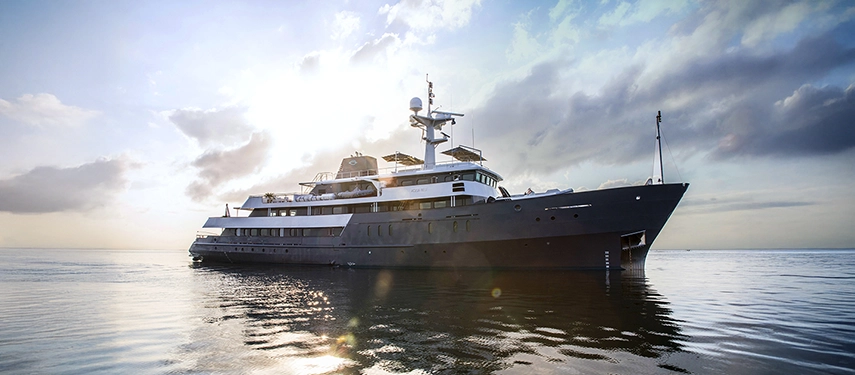 Aqua Blu gliding through serene tropical waters, sunlight glinting off her polished hull beneath a clear morning sky.