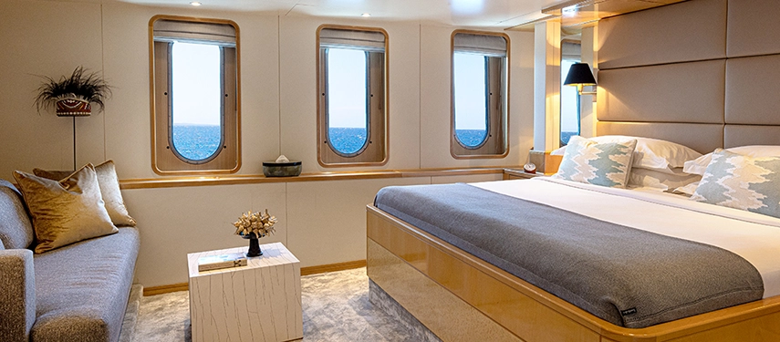 Bright ocean-view cabin with large porthole windows, king bed, and minimalist furnishings creating an atmosphere of calm sophistication.