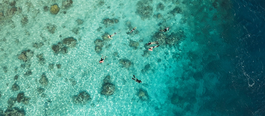 Snorkellers drift through shallow turquoise water above coral patches glowing beneath the Indonesian sun.