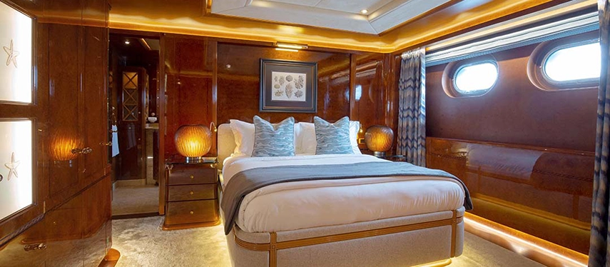 A serene stateroom aboard Aqua Mare featuring polished timber walls, ocean-view portholes and soft linens accented with sea-inspired cushions.