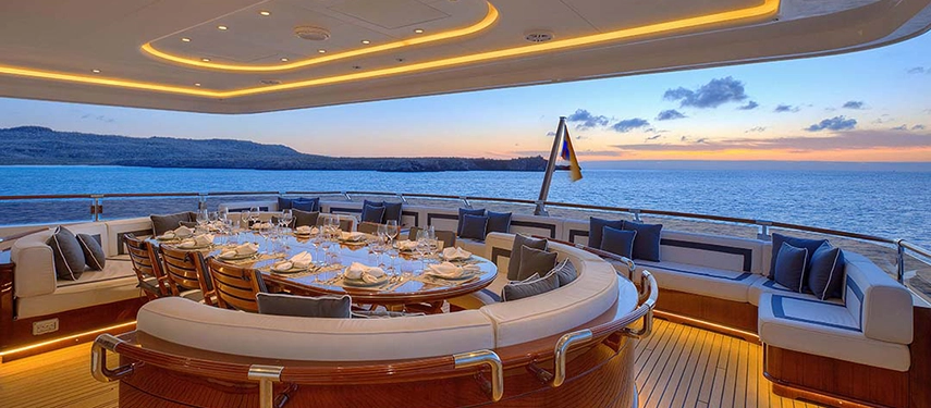 An elegant dining table is set on Aqua Mare’s aft deck, offering panoramic ocean views and golden evening light.