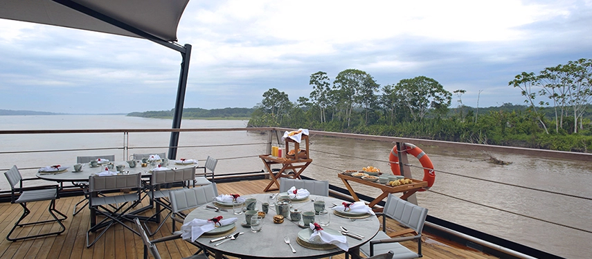Elegant al fresco dining setup on Aqua Nera’s deck, overlooking tranquil Amazon waters beneath overcast skies.