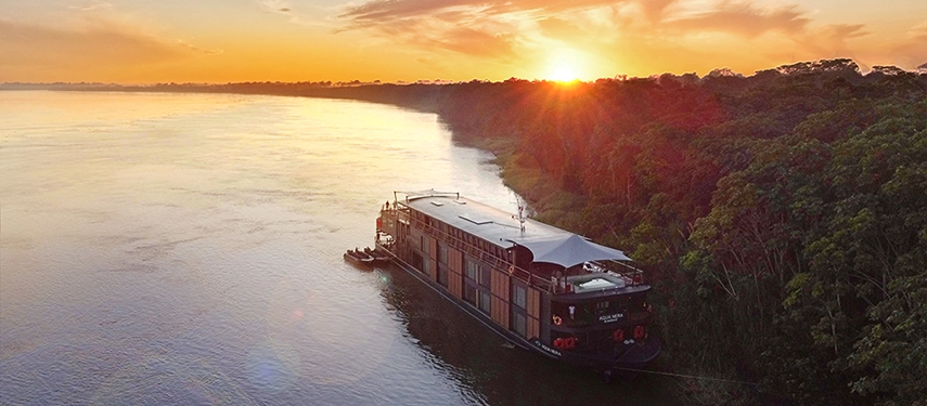 Aqua Nera anchored on the Amazon River at sunrise, its sleek design illuminated by soft golden light.