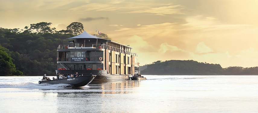 Aqua Nera cruising through the Amazon at sunset, accompanied by an excursion skiff gliding beside the vessel.