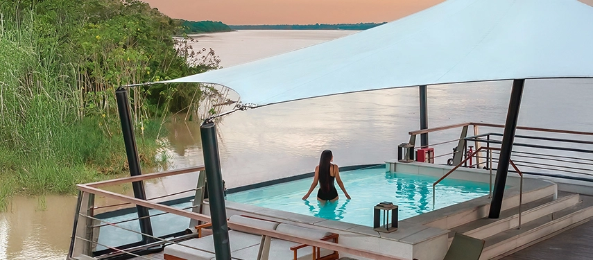 A woman relaxing in Aqua Nera’s plunge pool beneath a white canopy, gazing out over the Amazon River.