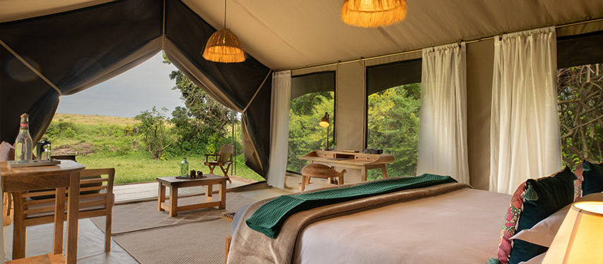 Inside a guest tent with a large bed, writing desk, and river views.