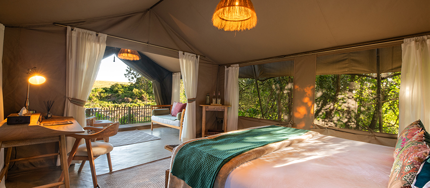 Inside view of a guest tent featuring a bed, writing desk, and open outlook onto the river landscape.