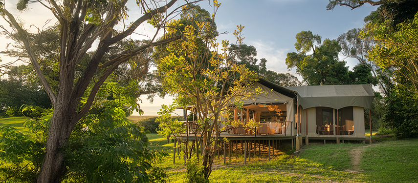 Side exterior of Rekero’s main tented area, set among open grassy glades and trees.