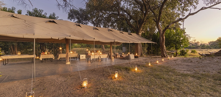 Canvas mess tent illuminated by lanterns at dusk, overlooking the bush setting of Kweene River Camp.