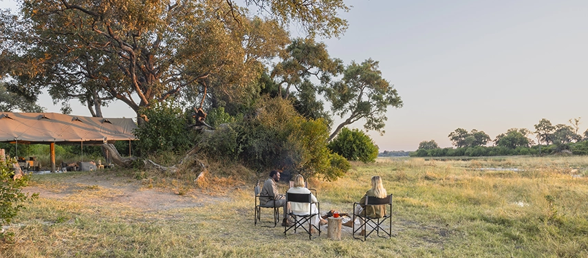 Guests gathered around a small campfire near the mess tent with sweeping Delta views at Kweene River Camp.