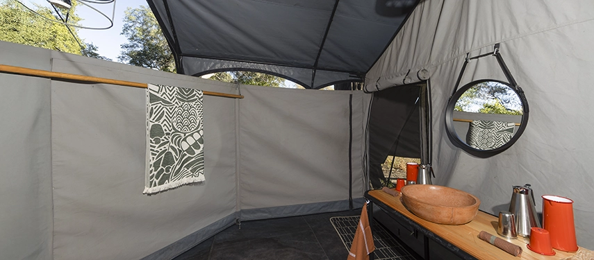 Safari tent bathroom with basin, mirror, canvas walls, and rustic wooden accents at Kweene River Camp.