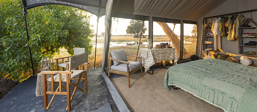 Interior of a Meru-style tent with bed, open wardrobe, and large windows looking onto the floodplains.