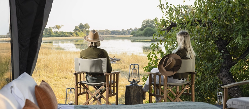 Couple enjoying Delta views from safari chairs on their private tent deck, seen from inside the room.