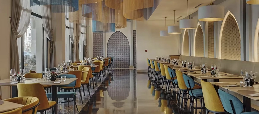 Spacious dining hall with polished floors, colourful chairs, and dramatic ceiling lights blending modern and Moroccan style.