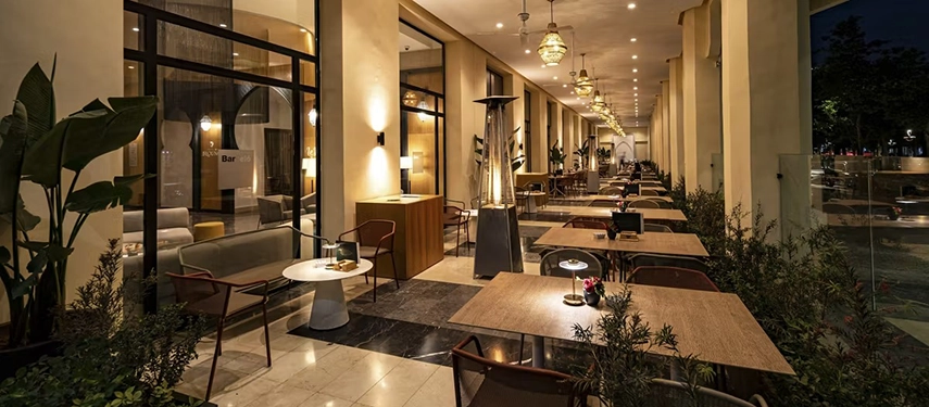 Cosy outdoor terrace dining space at night with warm lighting, heaters, and neatly arranged tables under covered arches.