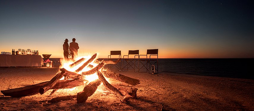 Guests gathered around a glowing campfire on the salt pans under a night sky.