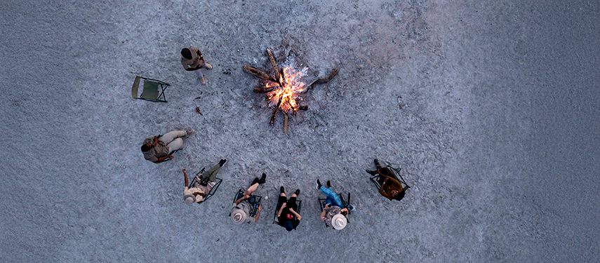 Aerial view of guests seated around a campfire on the vast Makgadikgadi salt pans.