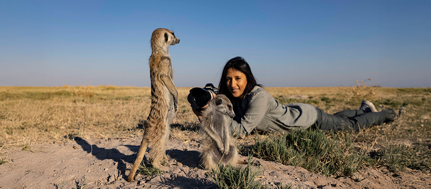 A woman photographs curious meerkats standing upright on the Makgadikgadi salt pans.