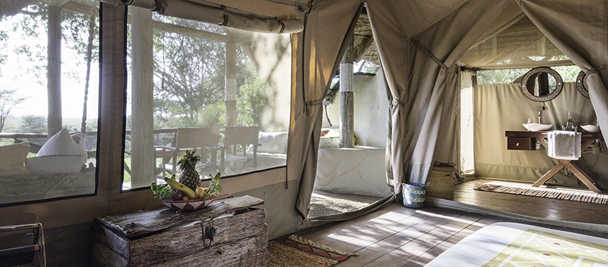 ight-filled luxury tent suite at Basecamp Masai Mara with canvas walls, polished wooden floors, and open-air en suite bathroom overlooking the bush.