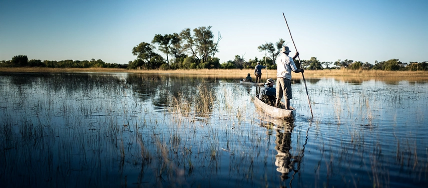 Guests explore the Okavango Delta by mokoro, gliding through reed-lined channels under wide African skies.