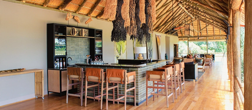 Open-air bar at Kanana Camp under a thatched roof with rustic decor and views over the plains.