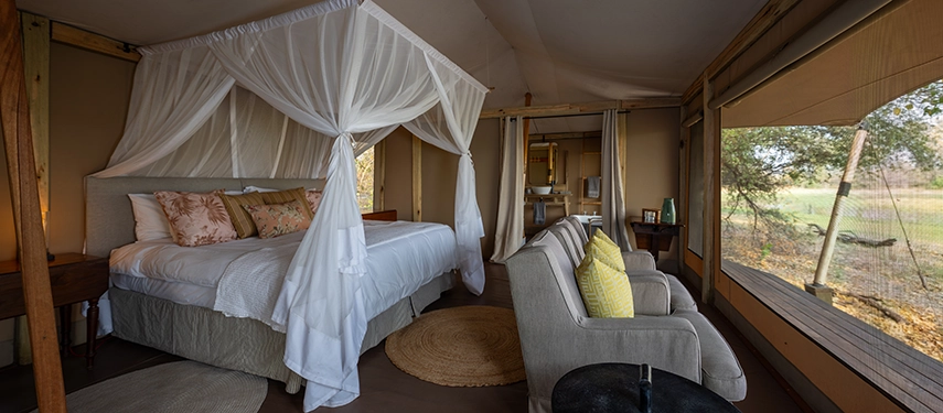 Interior of a tented suite with four-poster bed and open plan lounge.