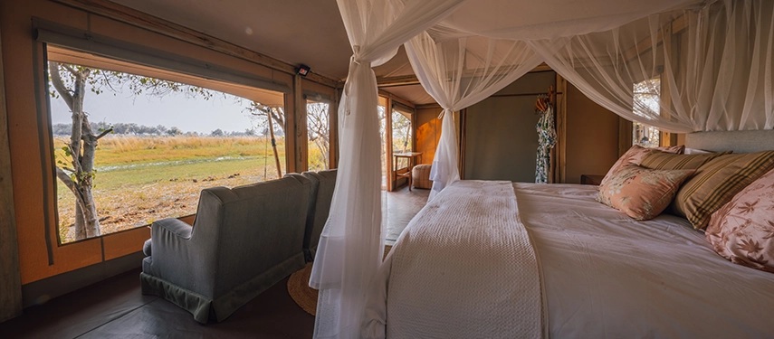 Bedroom at Cha Cha Metsi with canopy bed and lagoon views through wide windows.