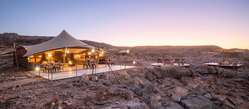 Open-air communal space at Camp Doros showcasing stylish safari furnishings and expansive views of the rocky terrain at sunset.