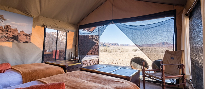 Cosy twin safari tent at Camp Sossus with open mesh walls revealing desert vistas and minimalistic safari-style decor.