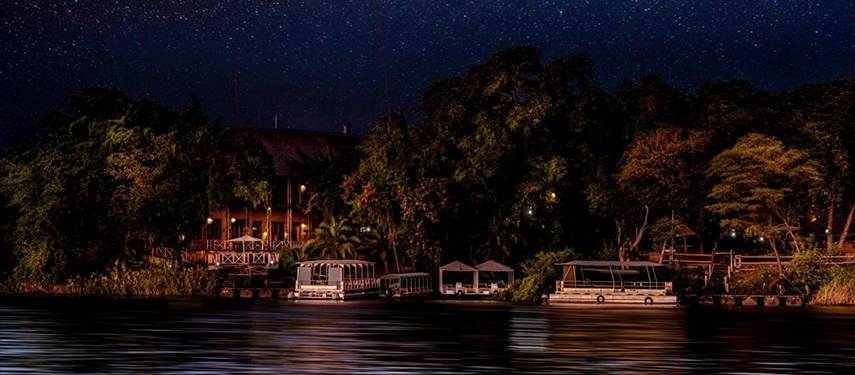 Night view of Chobe Marina Lodge with boats docked on the riverbank