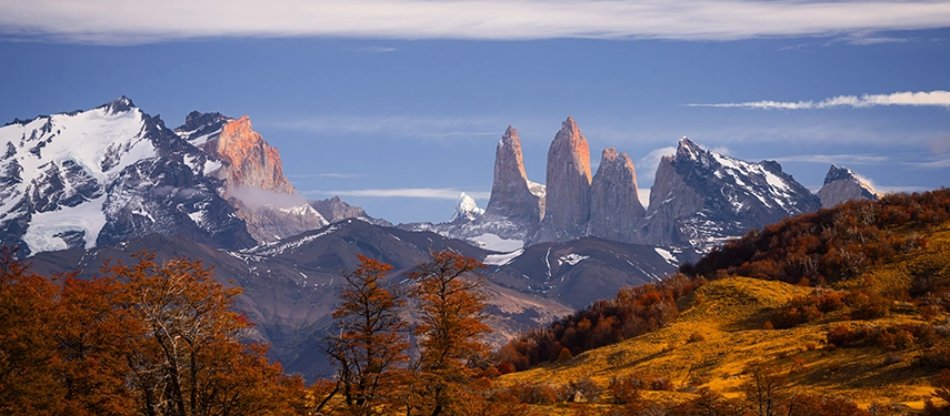 The iconic granite towers of Torres del Paine rise above autumnal forests and rolling foothills.