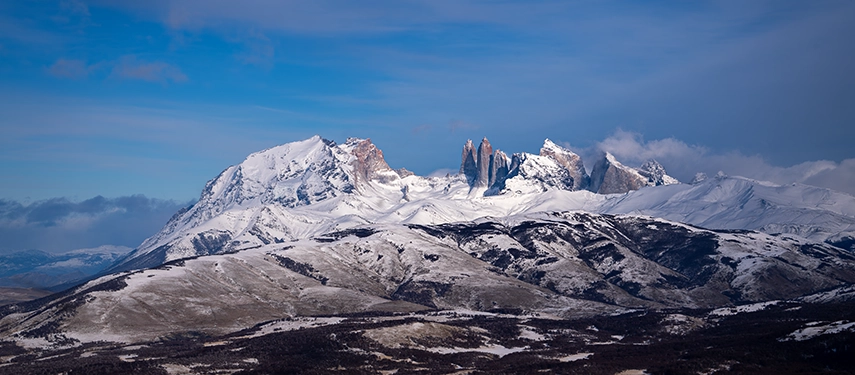 The iconic spires of Torres del Paine rise above a vast snow-covered landscape beneath a crisp blue sky.
