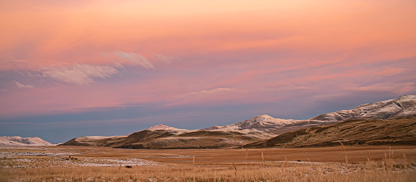 Soft pink light settles over wide Patagonian plains, revealing undulating hills lightly dusted with snow.