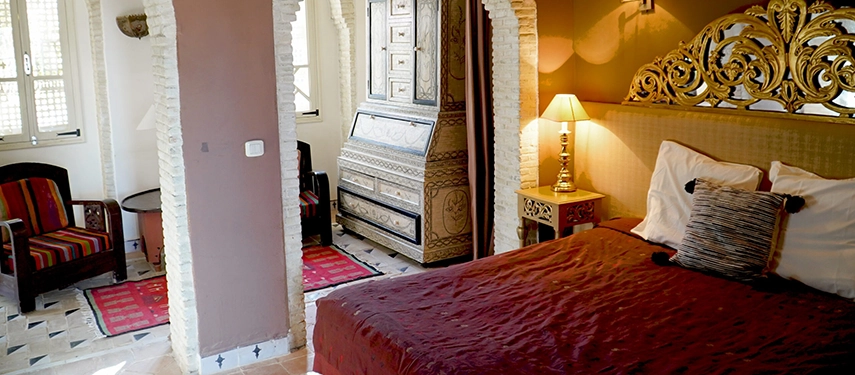 Elegant suite at Dar Tozeur with a carved wooden headboard, traditional furniture, and warm lighting.