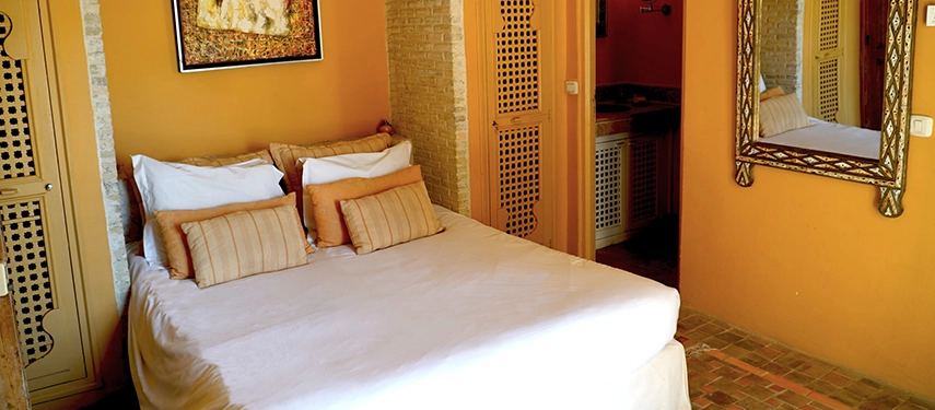 Cosy bedroom at Dar Tozeur with warm tones, a double bed, and ornate mirror.