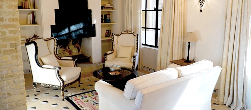 Bright sitting room at Dar Tozeur with cream armchairs, patterned floors, and a fireplace.
