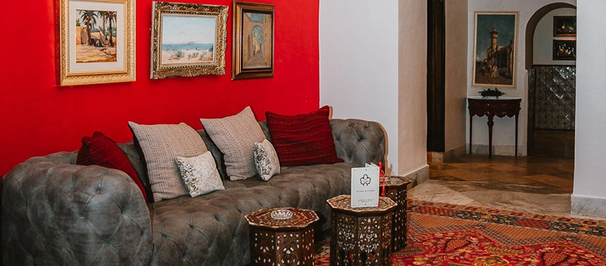 Charming lounge with red accent wall, vintage paintings, patterned carpet, and plush seating.