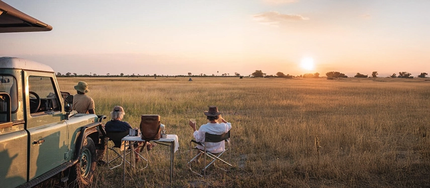 Guests enjoying sundowners beside their vehicle overlooking the Okavango plains.