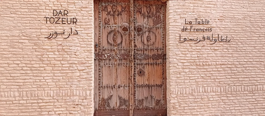 Close-up of Dar Tozeur’s main entrance door with signage for La Table de François in Arabic and French.